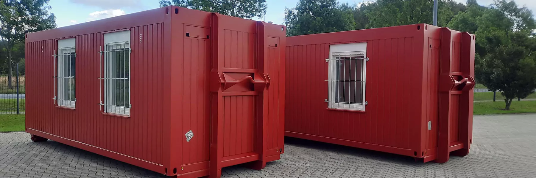 Zwei rote Abrollcontainer mit vergitterten Fenstern