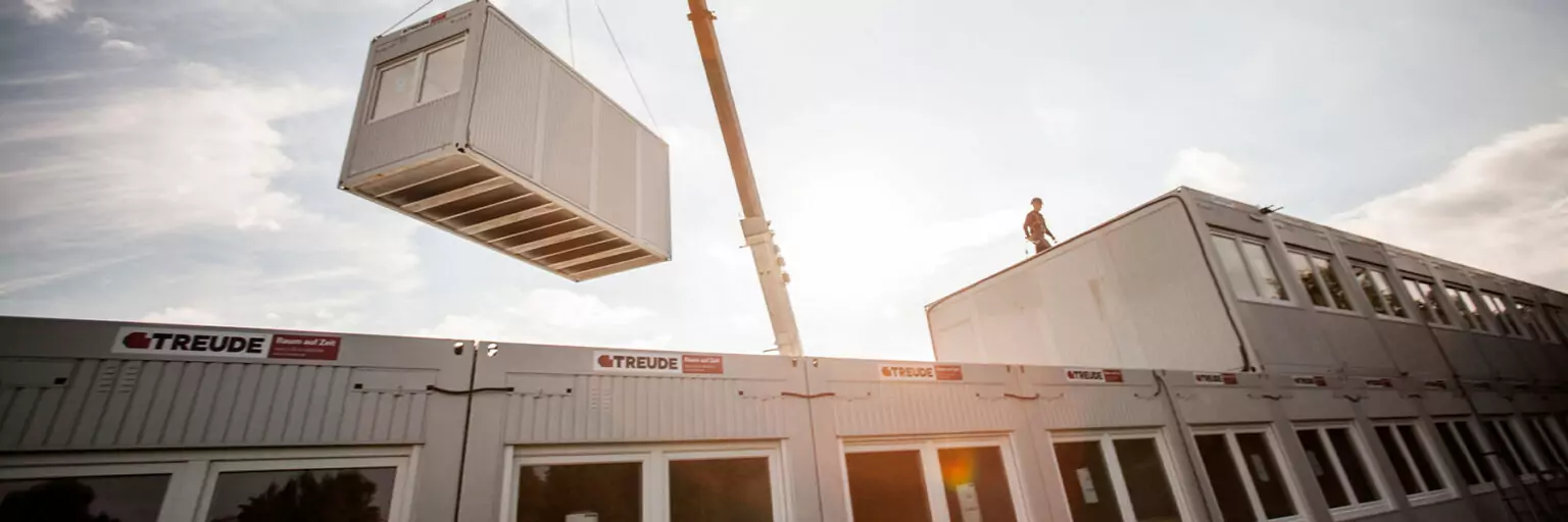 Ein Containermodul wird mit einem Kran auf eine Containeranlage gesetzt